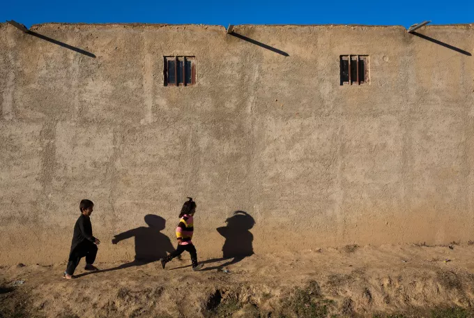 Two children create silhouettes as they run along tall bare wall