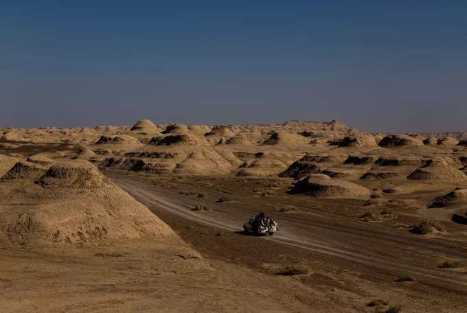 Image of a car with many passengers riding through a desert