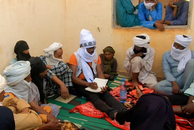 A group of men sit around a NRC member who is taking notes